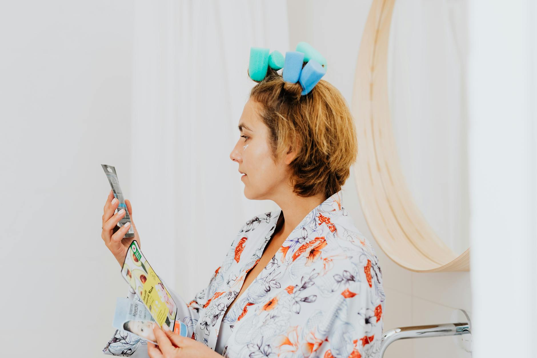 Kobieta w szlafroku z wałkami czyta instrukcję kosmetyku w domu