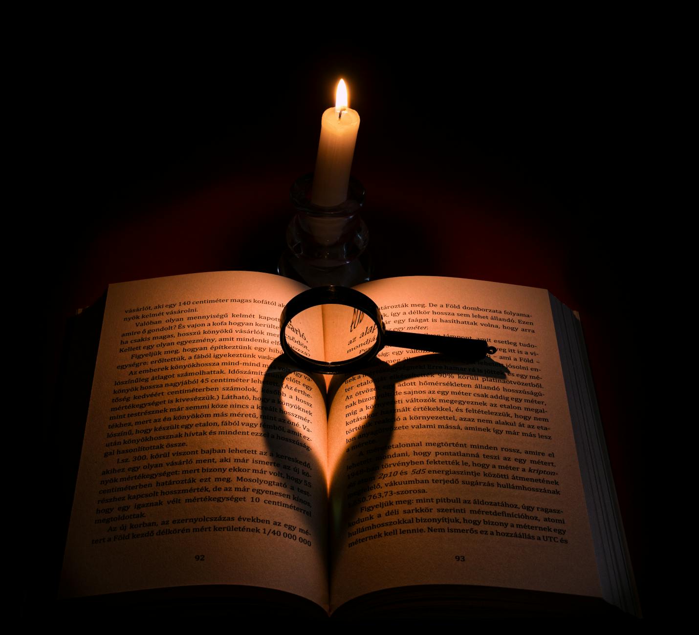 Książka oświetlona świecą i serce z cienia lupy jako symbol uwagi