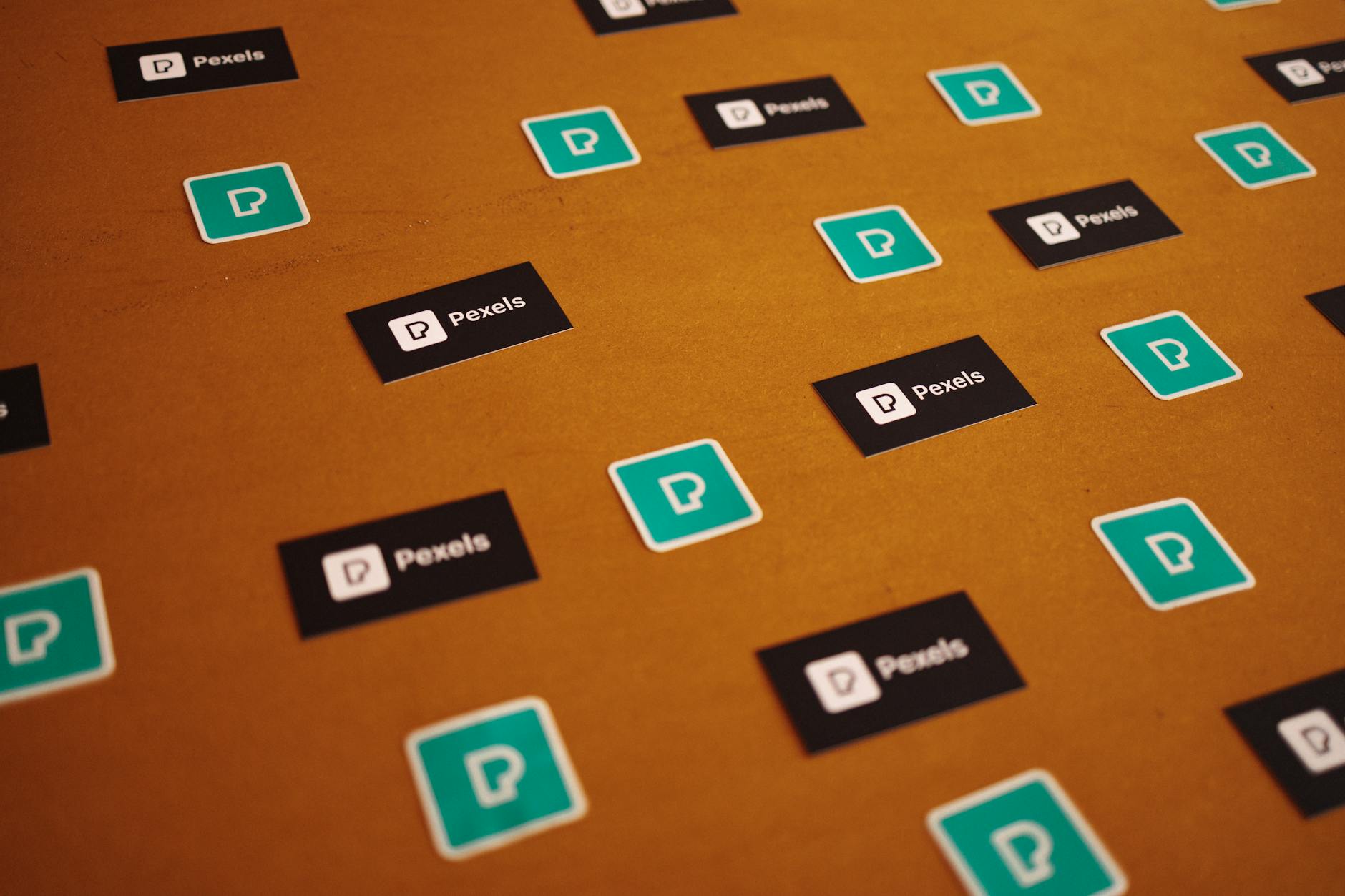 Naklejki z logo Pexels rozrzucone na brązowym tle
